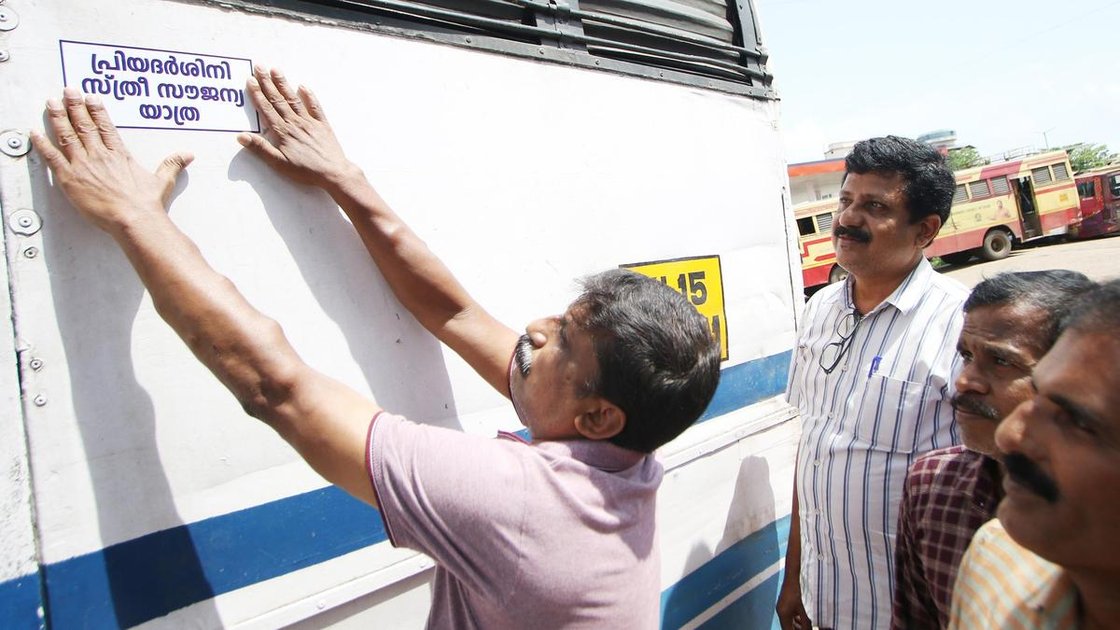 केरल की KSRTC बस पर प्रियदर्शिनी योजना का स्टिकर लगाते कर्मचारी