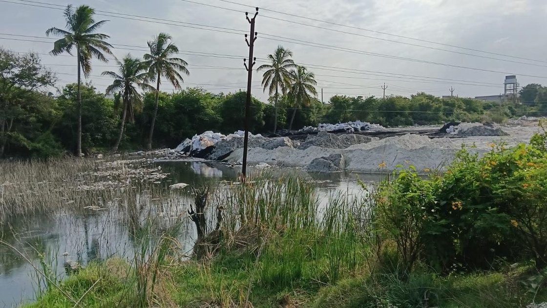 शूलागिरी आर्द्रभूमि में औद्योगिक कचरे का ढेर, जहां सफेद ग्रेनाइट धूल और काले कचरे के केक दिख रहे हैं
